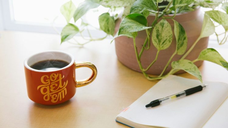 black retractable pen on opened book beside red and white go get'em-printed coffee cup